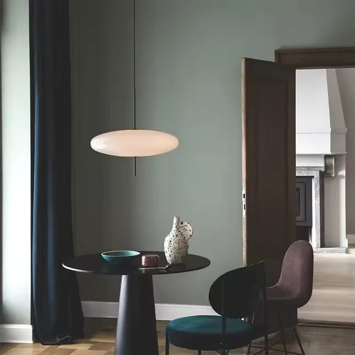 Lustre soucoupe volante blanc au design contemporain, suspendu au-dessus d’une table dans un intérieur élégant