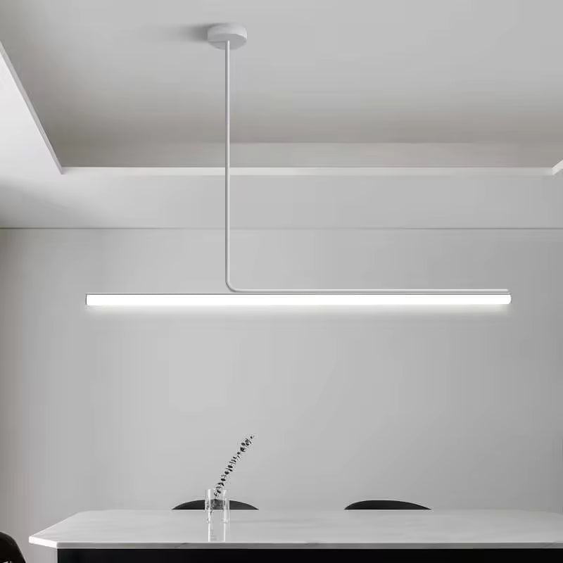 Dans un décor monochrome, ce lustre tube avec structure en métal blanc dessine une ligne lumineuse sobre au-dessus d’une grande table.