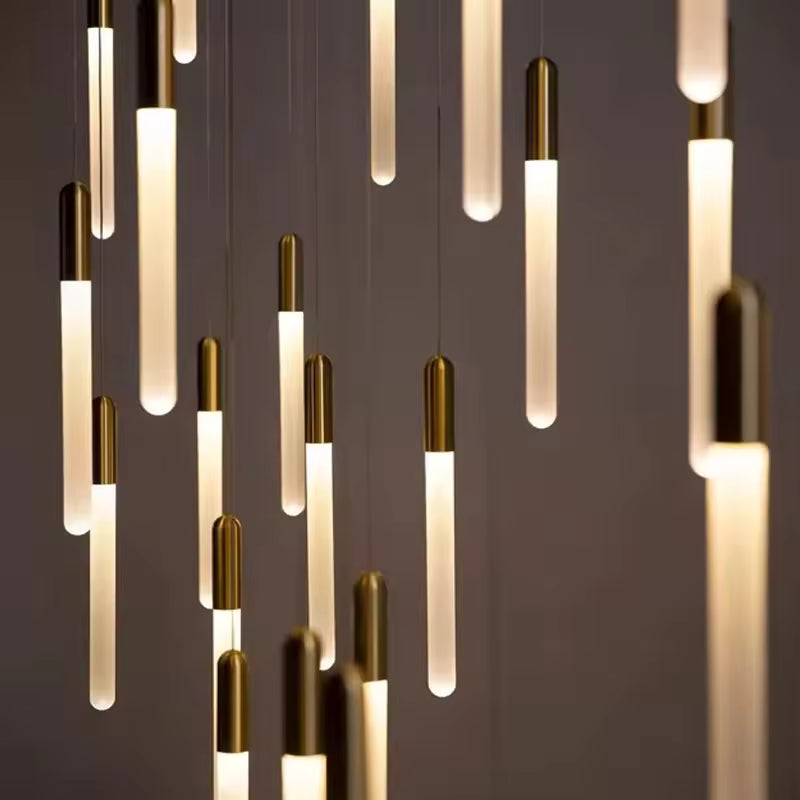 En cascade, les tubes lumineux dorés forment un lustre élancé au rythme vertical et à l’allure sophistiquée