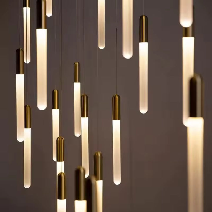 En cascade, les tubes lumineux dorés forment un lustre élancé au rythme vertical et à l’allure sophistiquée