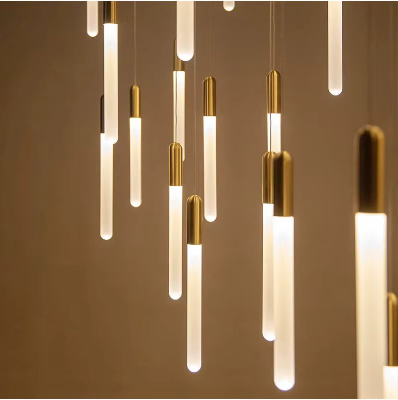 Une multitude de tubes lumineux dorés forme une suspension graphique au rythme vertical et au style contemporain