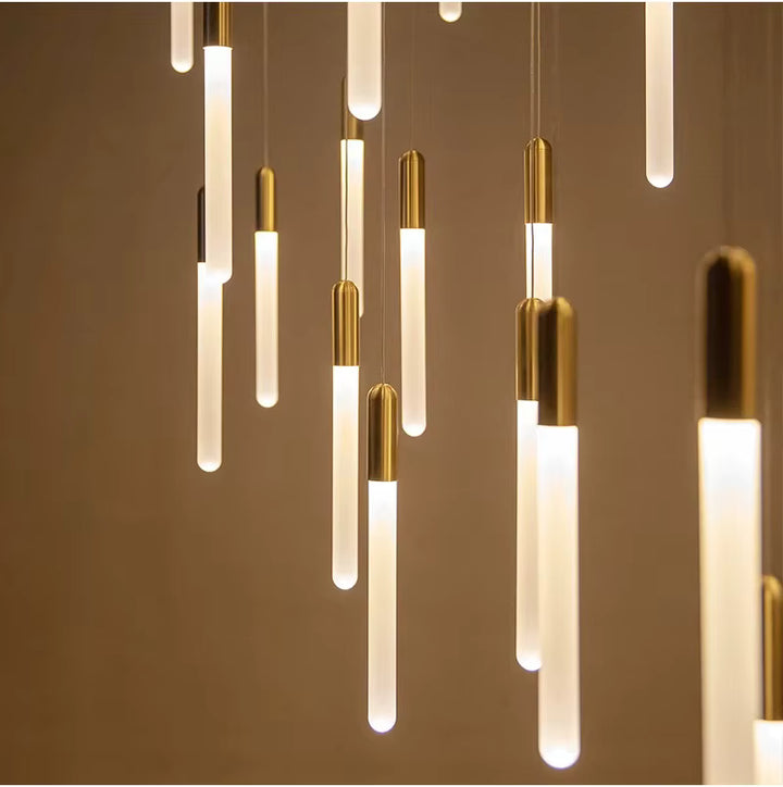 Une multitude de tubes lumineux dorés forme une suspension graphique au rythme vertical et au style contemporain