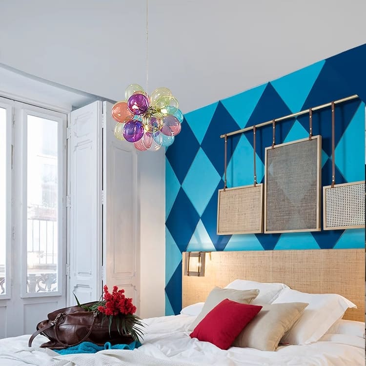 Lustre contemporain en verre translucide multicolore illuminant une chambre aux murs géométriques bleus.