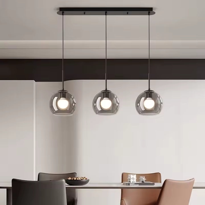 Dans un décor épuré, ce lustre à trois globes fumés apporte une touche moderne au-dessus de la table
