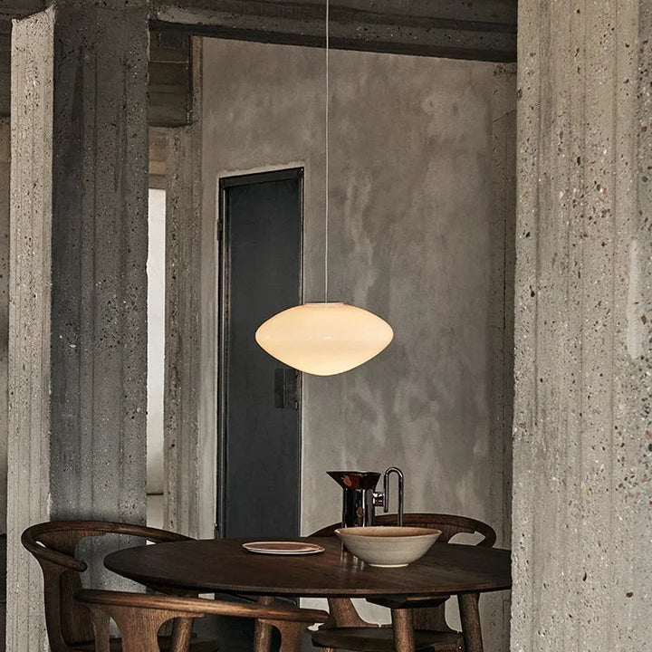 Lustre moderne en verre opalin diffusant une lumière chaleureuse dans un salon au décor industriel.