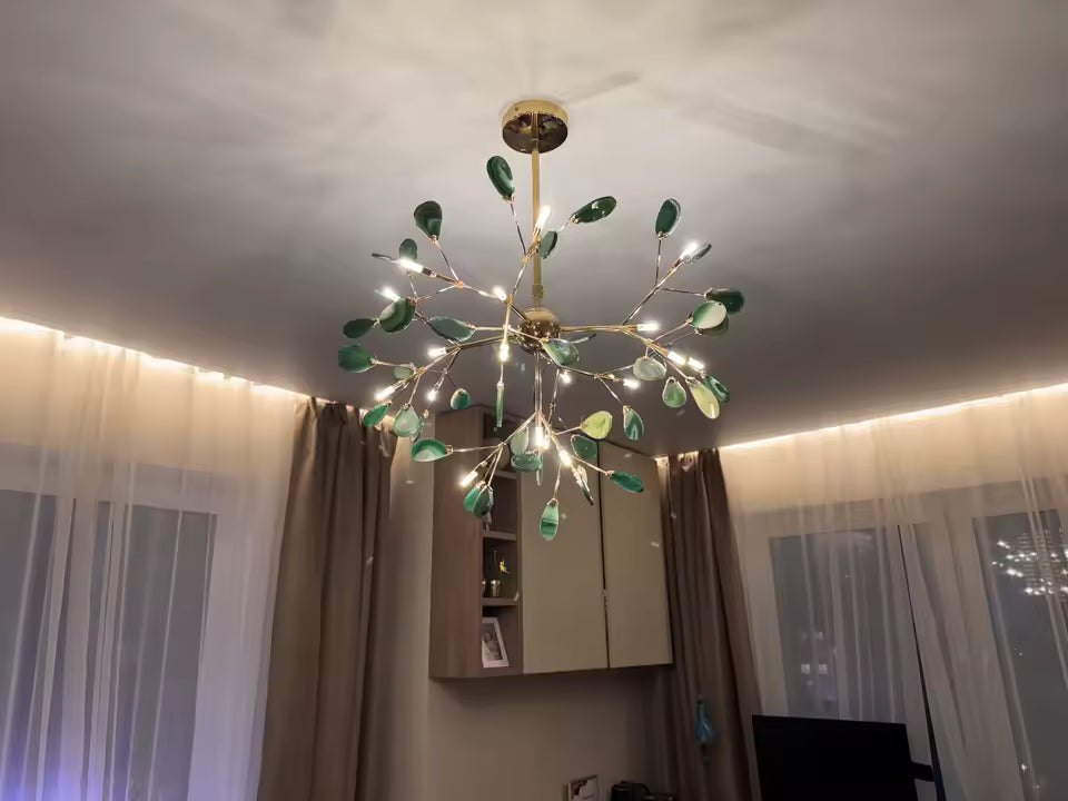 Lustre vert en agate naturelle illuminé, aux branches dorées et feuillages minéraux dans un intérieur contemporain