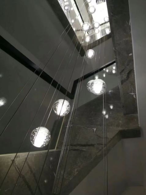 Lustre vertical de globes en verre bullé dans escalier en pierre, éclairage architectural contemporain et élégant.