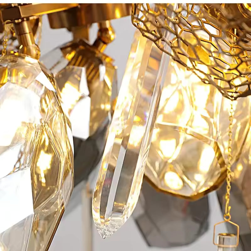 Détail d’une pampille en cristal transparent aux côtés des facettes fumées et de la structure dorée du lustre sculptural.
