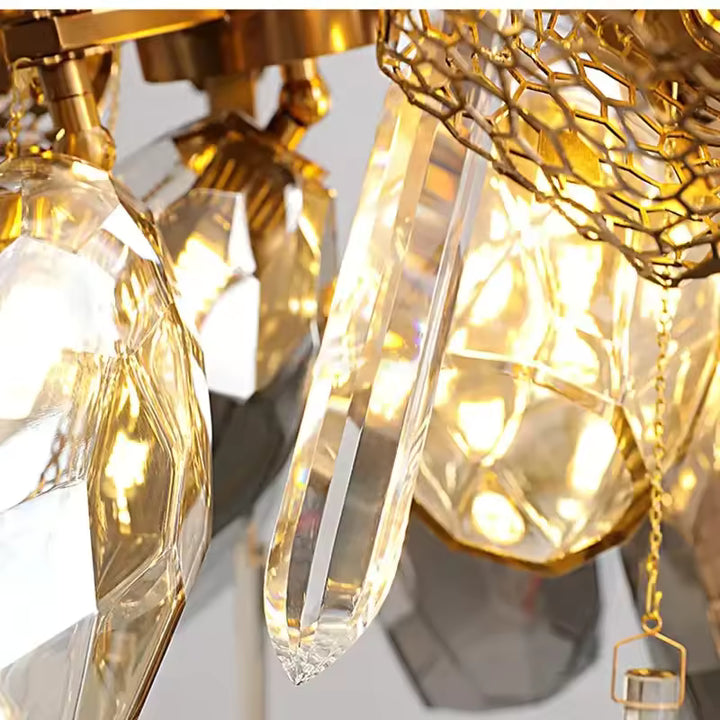 Détail d’une pampille en cristal transparent aux côtés des facettes fumées et de la structure dorée du lustre sculptural.