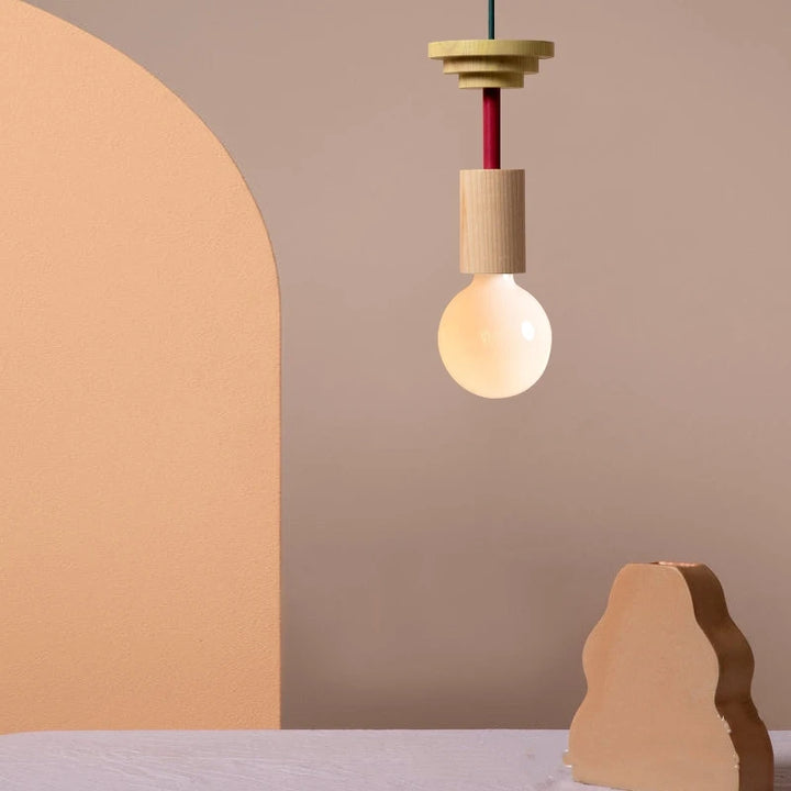 Petite suspension géométrique en bois coloré suspendue dans un intérieur minimaliste.