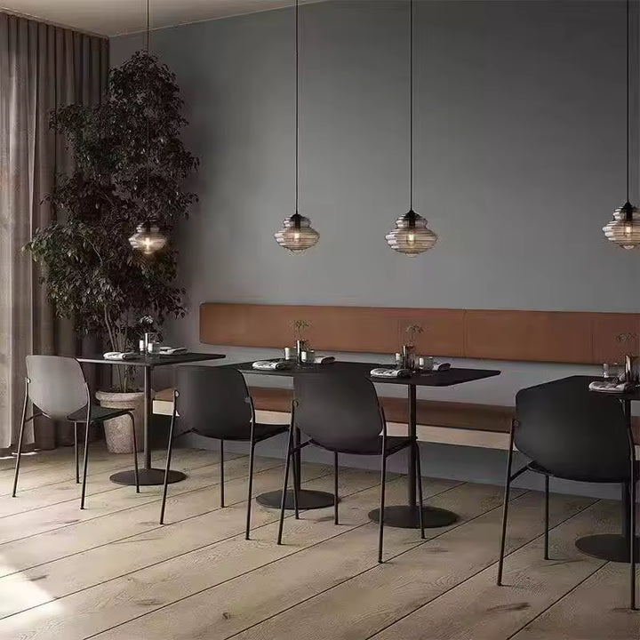 Petites suspensions en verre fumé aux reliefs concentriques, alignées au-dessus de tables dans un restaurant contemporain.
