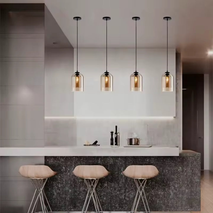Quatre suspensions en verre ambré aux lignes arrondies illuminent un îlot de cuisine dans un esprit contemporain chic.