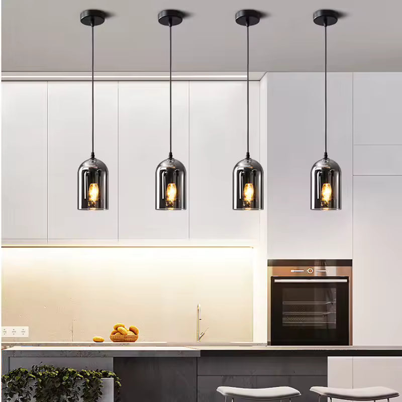 Alignées dans une cuisine épurée, quatre suspensions en verre fumé aux reflets chromés offrent un éclairage chaleureux et design.