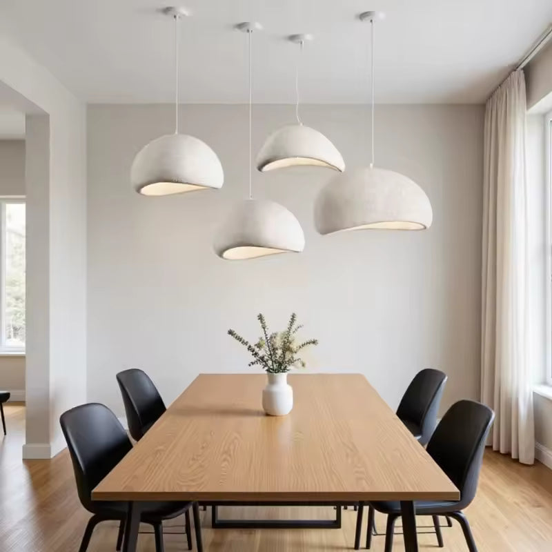 Quatre suspensions blanches aux dômes irréguliers habillent une salle à manger épurée, entre design organique et minimalisme.