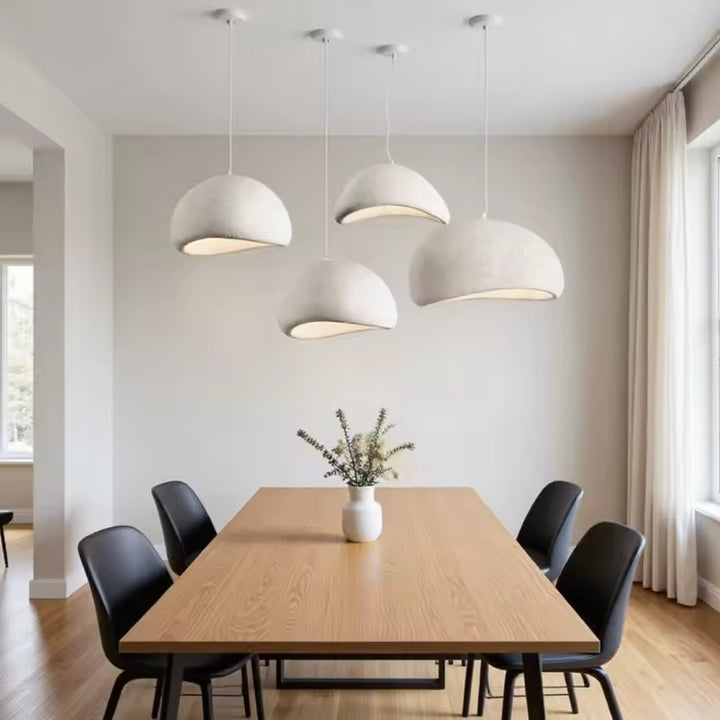 Quatre suspensions blanches aux dômes irréguliers habillent une salle à manger épurée, entre design organique et minimalisme.