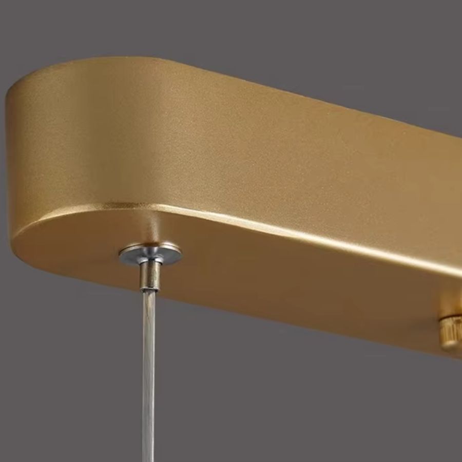 Détail de la rosace dorée et du câble fin d’une suspension design aux finitions modernes et minimalistes