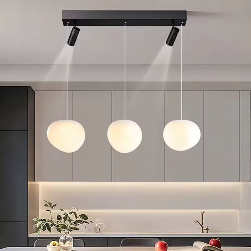 Éclairage minimaliste à trois globes opalins suspendus et deux spots orientables sur barre noire