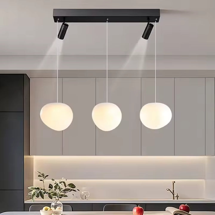 Éclairage minimaliste à trois globes opalins suspendus et deux spots orientables sur barre noire
