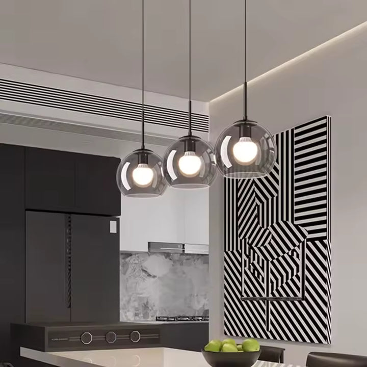 Éclairage contemporain avec trois globes en verre fumé et ampoules visibles au-dessus d’une cuisine moderne
