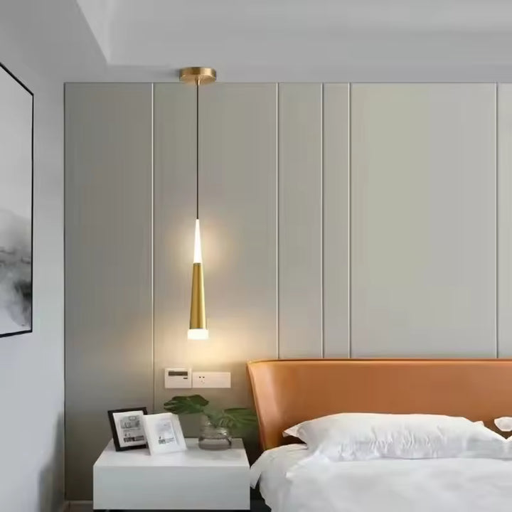 Près du lit, une suspension aiguille LED dorée diffuse une lumière douce dans une chambre moderne et épurée