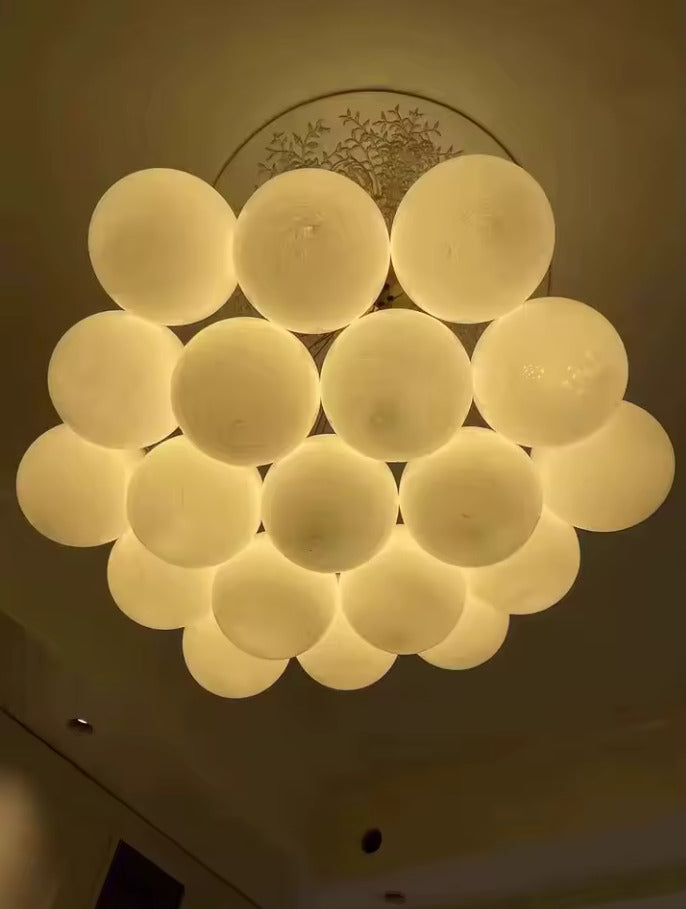 Suspension allumée en grappe de globes en verre opalin diffusant une lumière chaude et homogène dans un intérieur moderne.