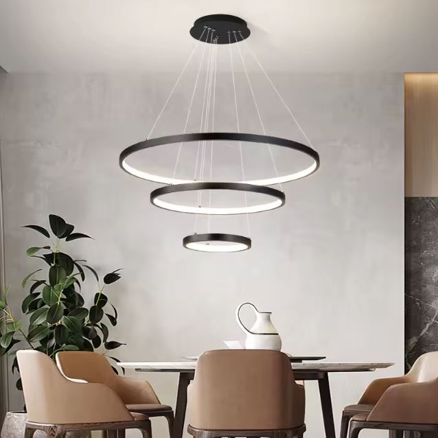 Suspension anneau LED noire à trois rangs avec plante en fond, parfaite pour illuminer élégamment une salle à manger.