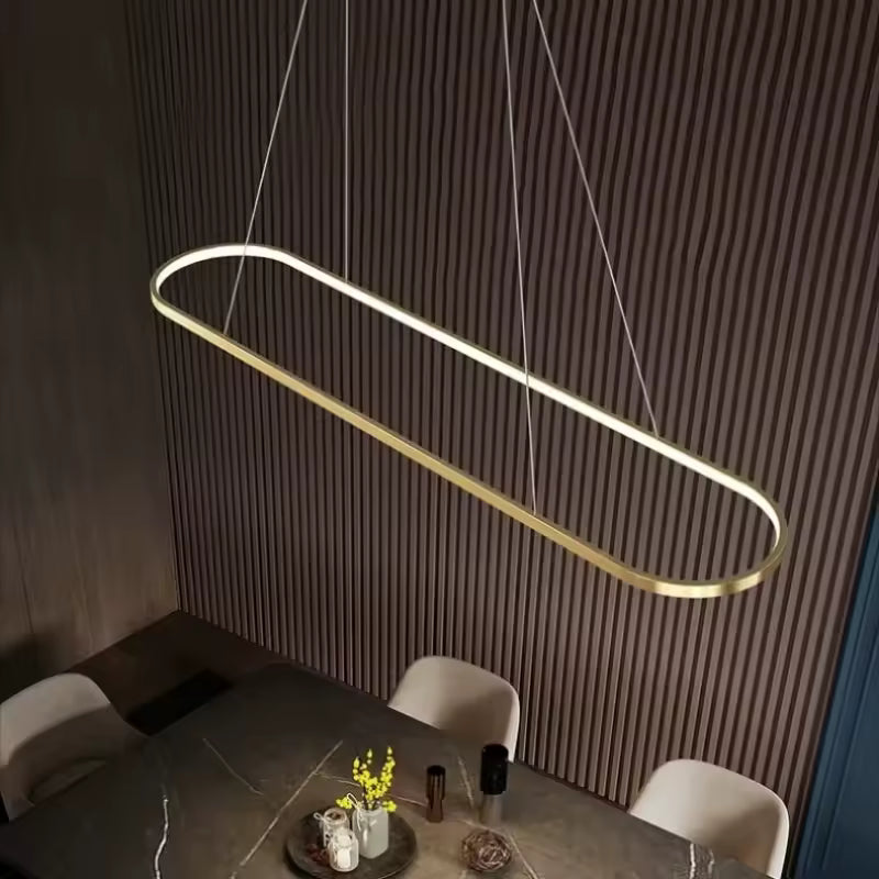 Au-dessus d’une table, cette suspension LED dorée en anneau rectangulaire aux angles arrondis affirme un style minimaliste