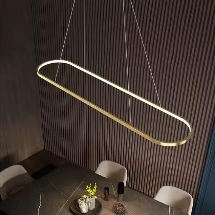 Au-dessus d’une table, cette suspension LED dorée en anneau rectangulaire aux angles arrondis affirme un style minimaliste
