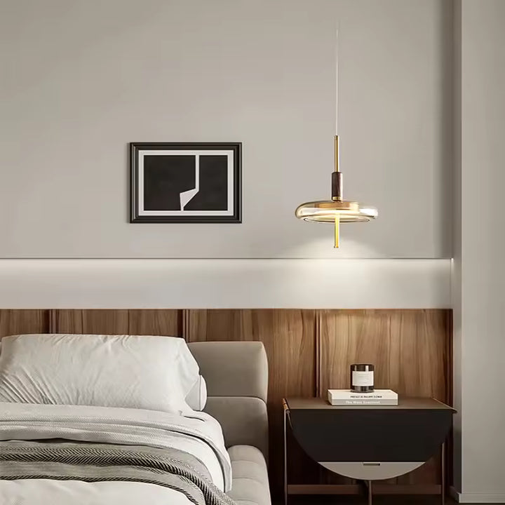 Suspension à anneau de verre et tige dorée au style contemporain, installée en éclairage de chevet dans une chambre