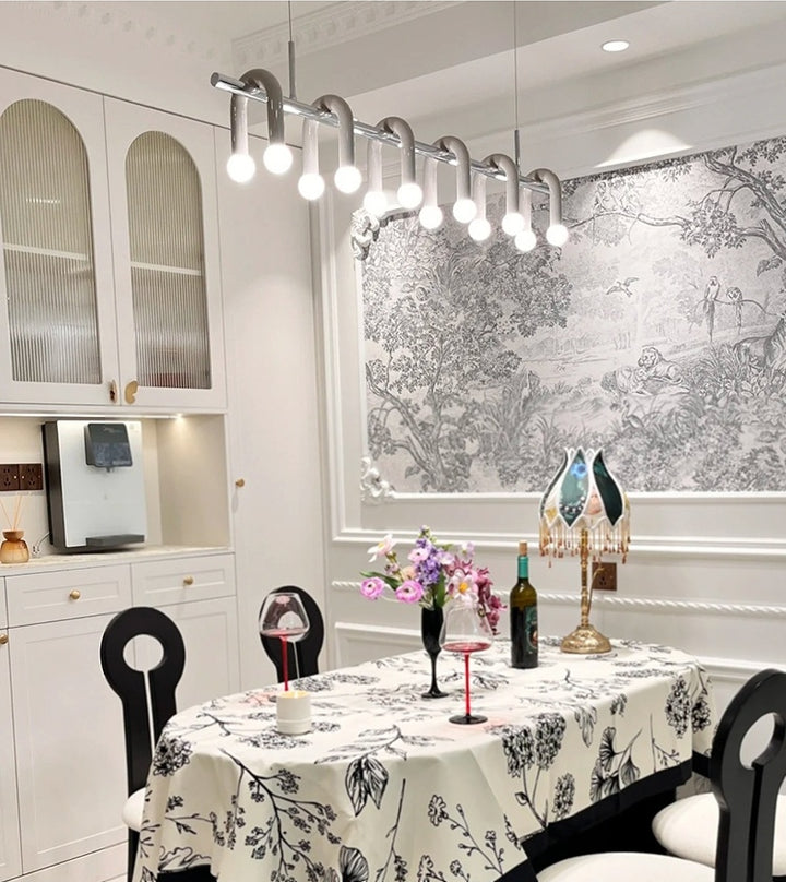 Ambiance de salle à manger chic éclairée par une suspension linéaire blanche à arches et globes.