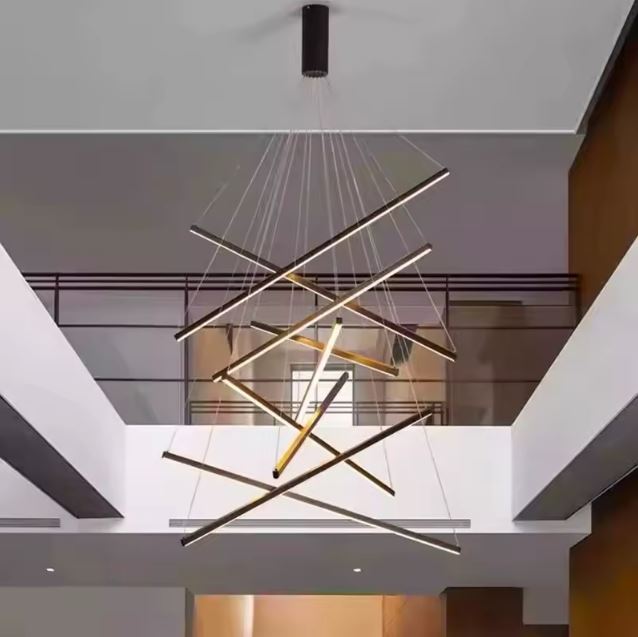 Suspension LED graphique composée de tiges croisées, suspendue dans un vide sur séjour moderne ou une cage d’escalier ouverte.
