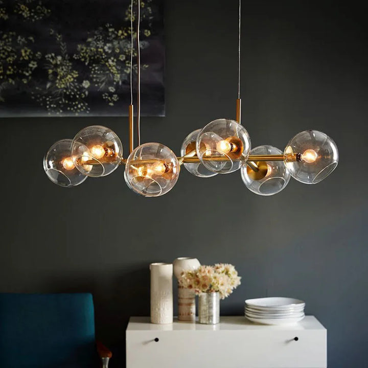 Suspension constellation style art déco revisité à structure en laiton et globes de verre transparent sur fond de mur sombre.