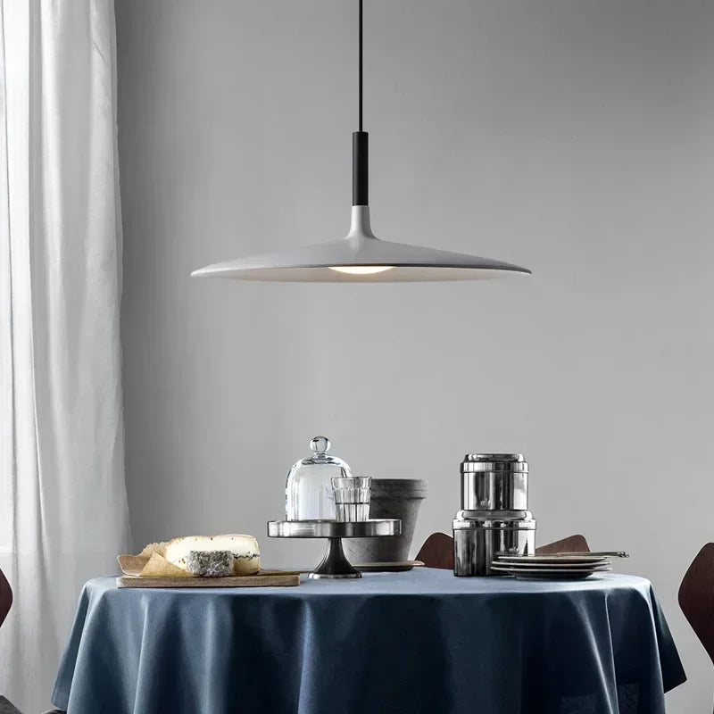 Suspension grise en forme d'aile évasée au-dessus d'une table dressée dans une salle à manger moderne.