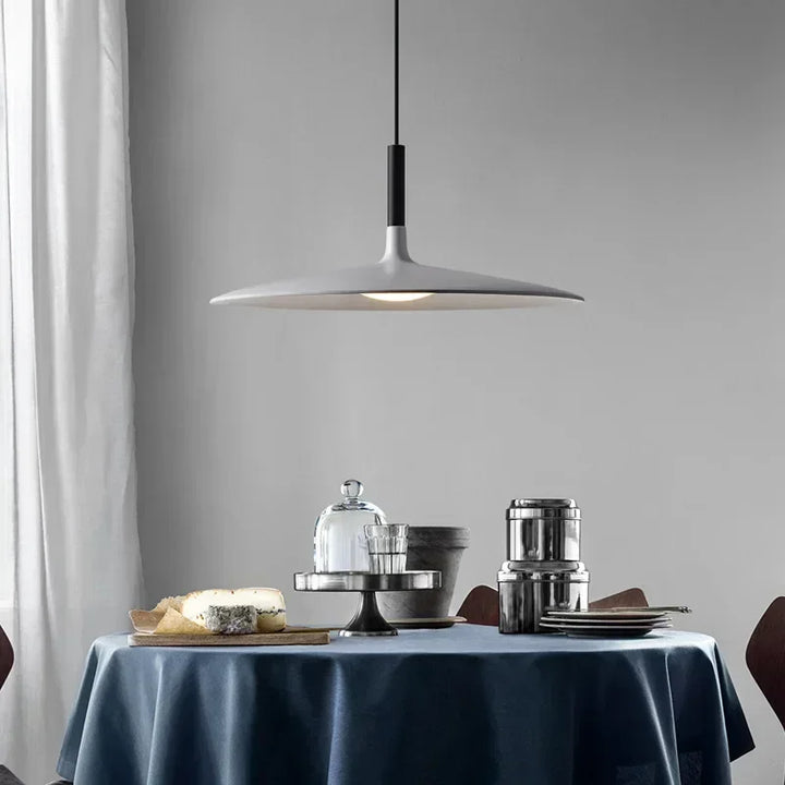 Suspension grise en forme d'aile évasée au-dessus d'une table dressée dans une salle à manger moderne.