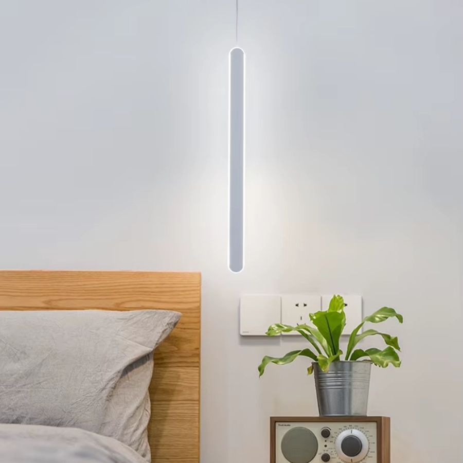 Fine et lumineuse, cette suspension blanche verticale accompagne un chevet au style scandinave épuré