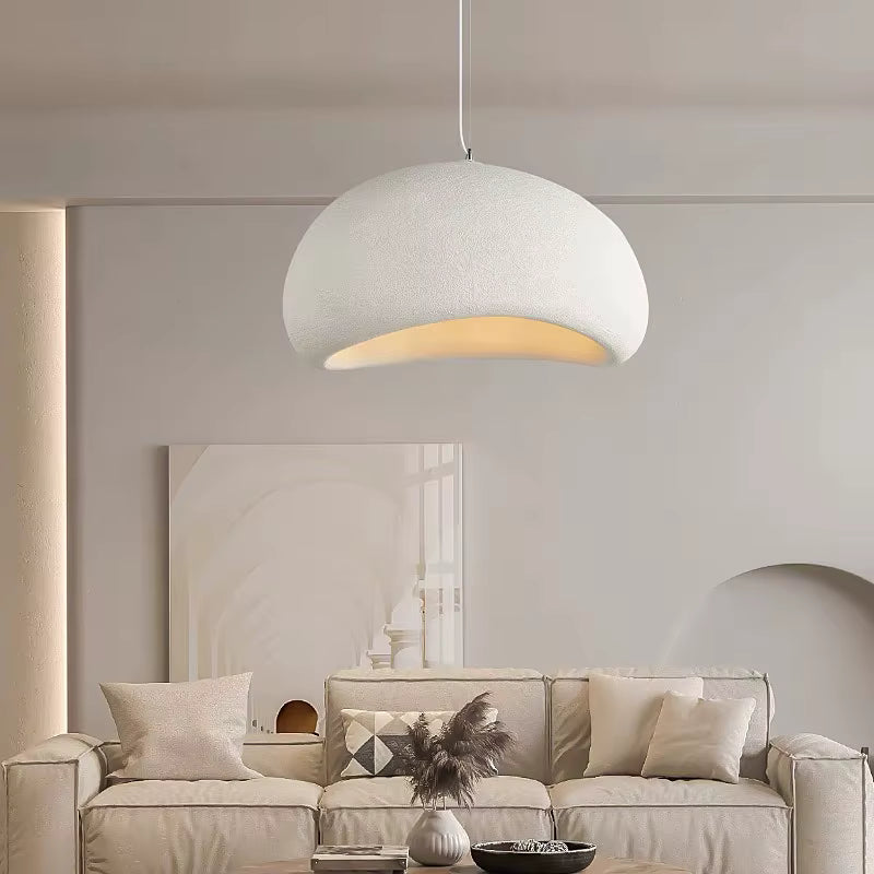 Une suspension wabi-sabi blanche au dôme asymétrique et texturé illumine un salon minimaliste aux tons beiges et naturels.