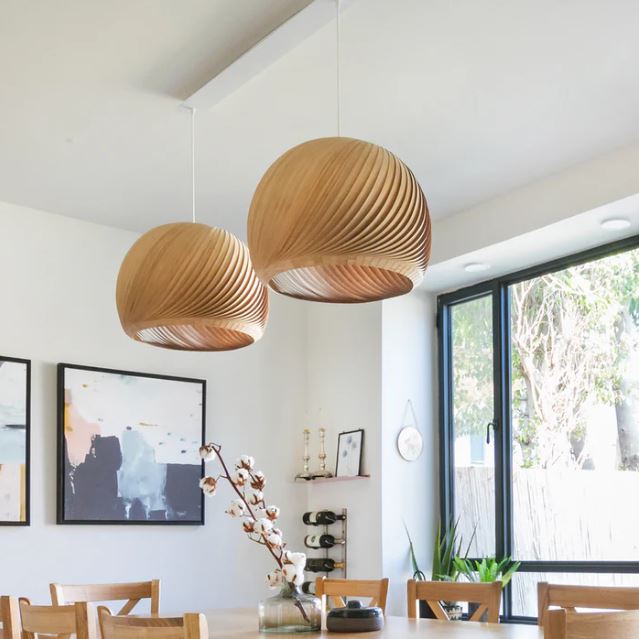 Suspension boule bois au design moderne dans une salle à manger lumineuse avec des fenêtres grandes ouvertes et une table en bois clair.