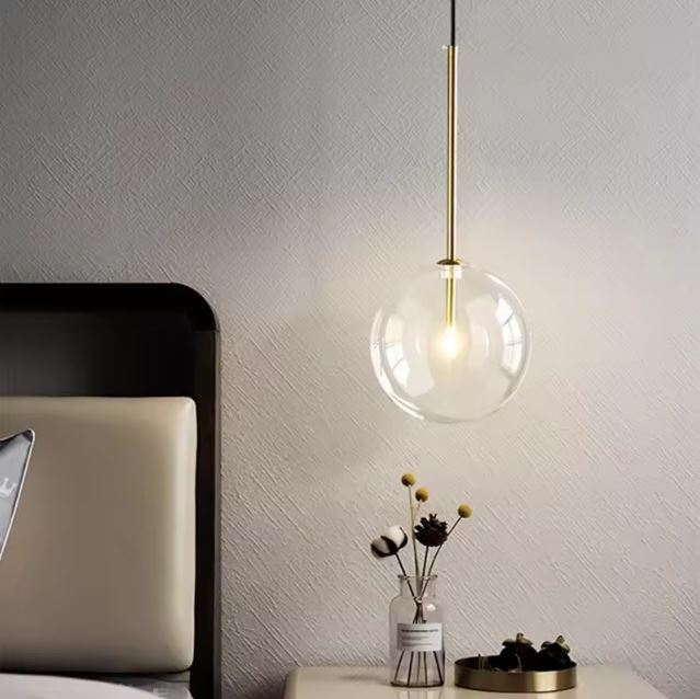 Suspension boule en verre transparent avec finition en laiton, idéale pour un éclairage doux et moderne dans un salon ou chambre à coucher.