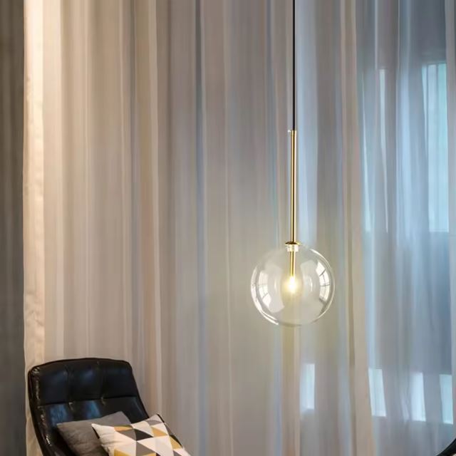 Élégante suspension boule en verre transparent avec support en laiton, idéale pour un éclairage subtil et moderne dans un salon ou chambre.