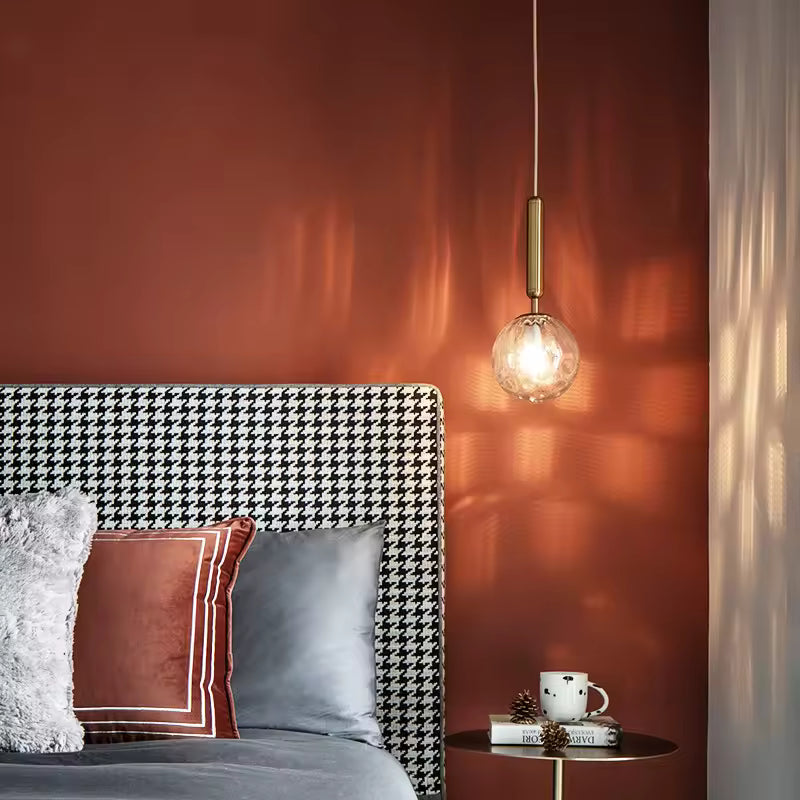 Suspension boule en verre sculpté avec tige dorée, installée en chevet dans une chambre élégante aux accents rétro chic
