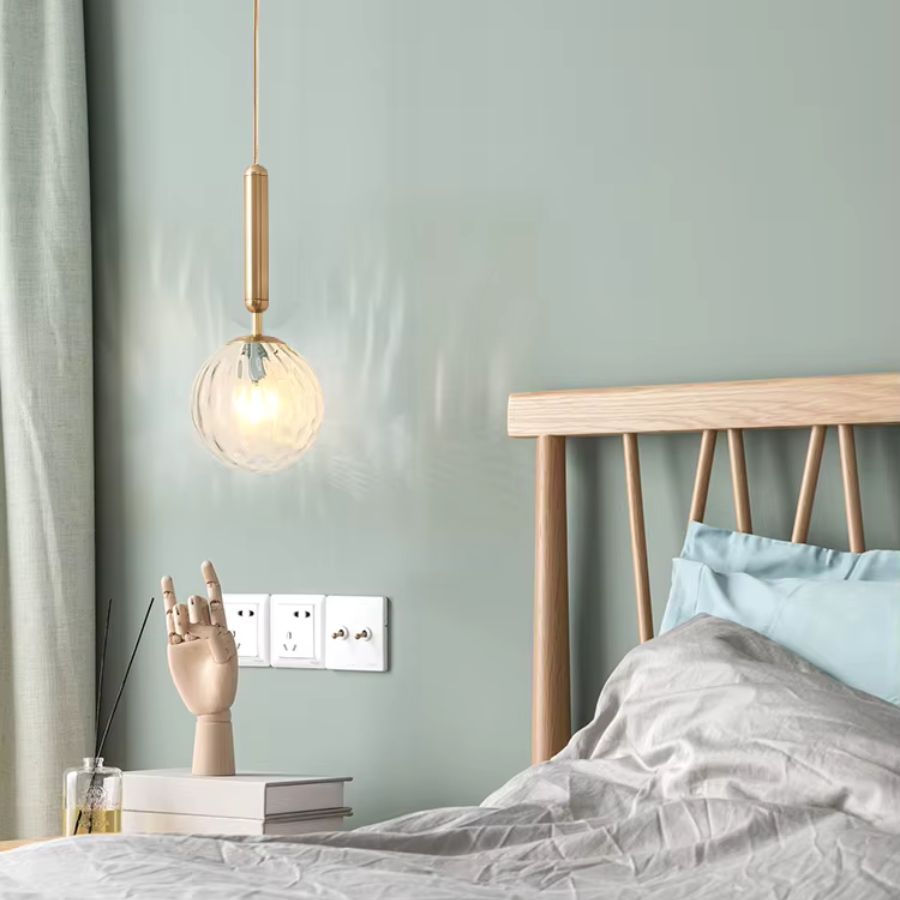 Suspension boule en verre transparent à tige dorée, utilisée en chevet dans une chambre douce au style scandinave et épuré