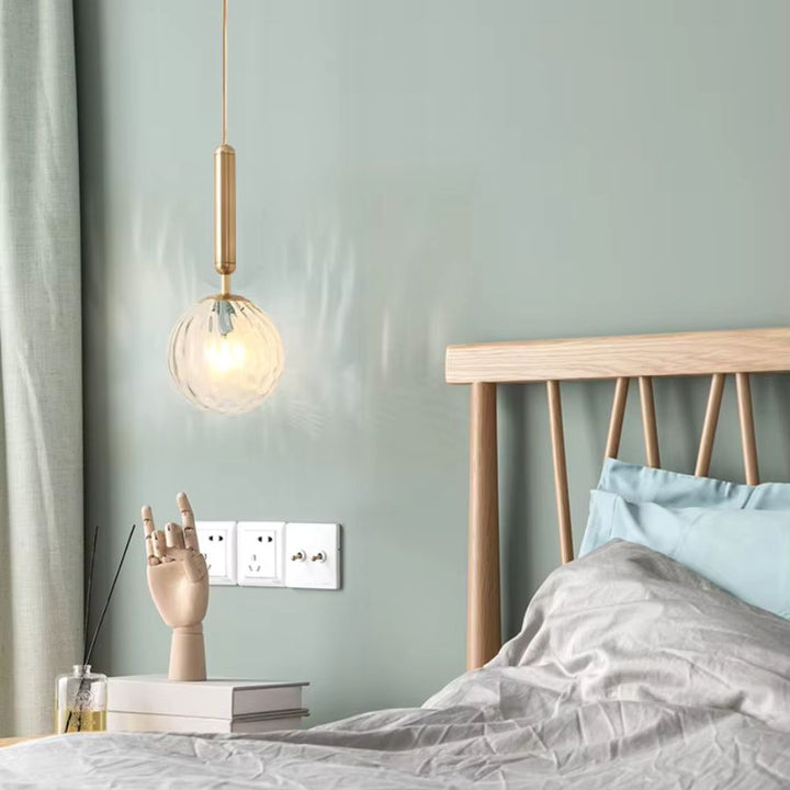Suspension boule en verre transparent à tige dorée, utilisée en chevet dans une chambre douce au style scandinave et épuré