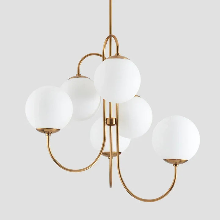 Vue studio de la suspension à six branches en laiton doré et globes en verre opalin blanc sur fond gris clair.