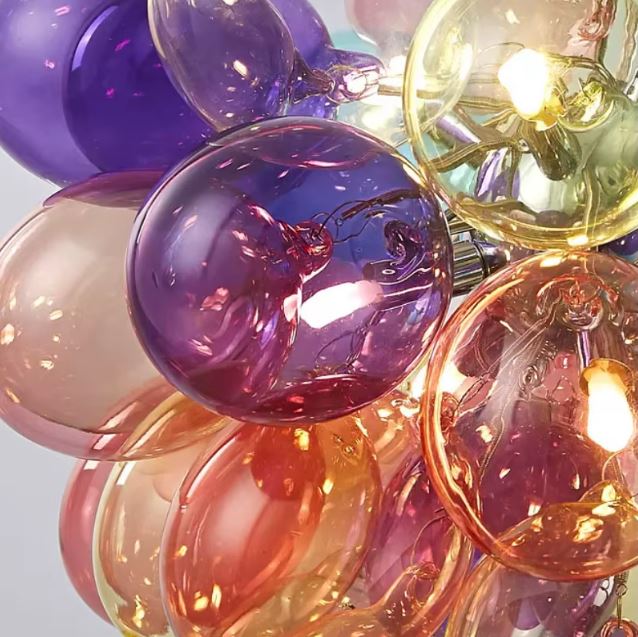 Gros plan sur les globes en verre coloré d'une suspension design, révélant des reflets irisés aux accents rétro et artistiques.