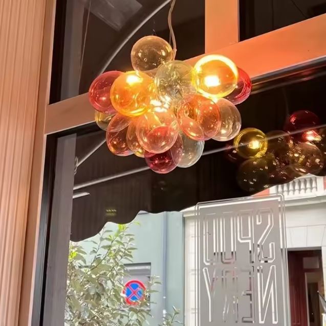 Suspension en globes de verre coloré translucide illuminés, créant un bouquet lumineux au charme rétro et artistique.
