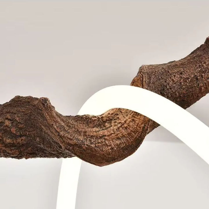 Détail d'une suspension sculpturale effet branche d'arbre, avec écorce texturée marron et néon LED blanc entrelacé.