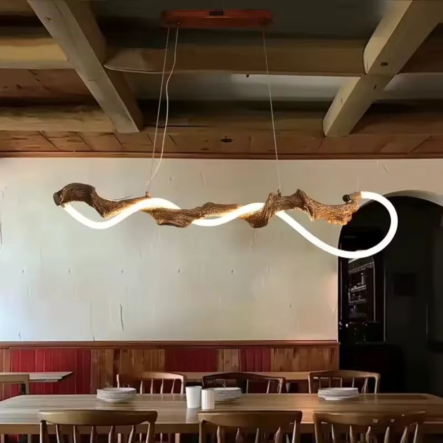 Au-dessus d'une grande table, suspension sculpturale en métal effet branche d'arbre, traversée d'un néon LED sinueux.