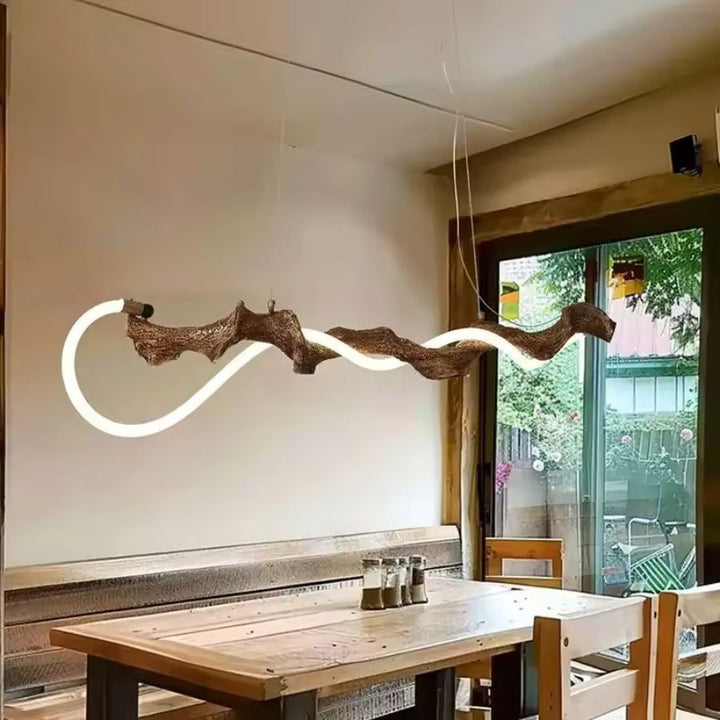 Suspension en métal imitation branche d'arbre enlacée d'un néon LED ondulé, au-dessus d'une table en bois rustique.