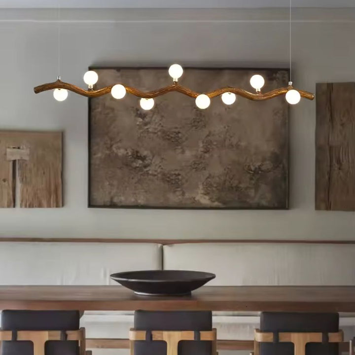 Dans une salle à manger wabi-sabi, suspension linéaire effet bois à branche sinueuse et globes blancs lumineux.