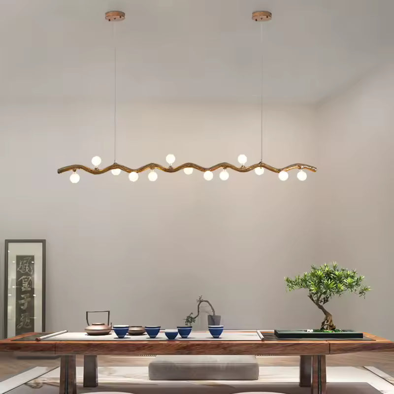 Une longue suspension effet bois aux courbes naturelles et globes blancs éclaire une table basse dans un décor zen japandi.